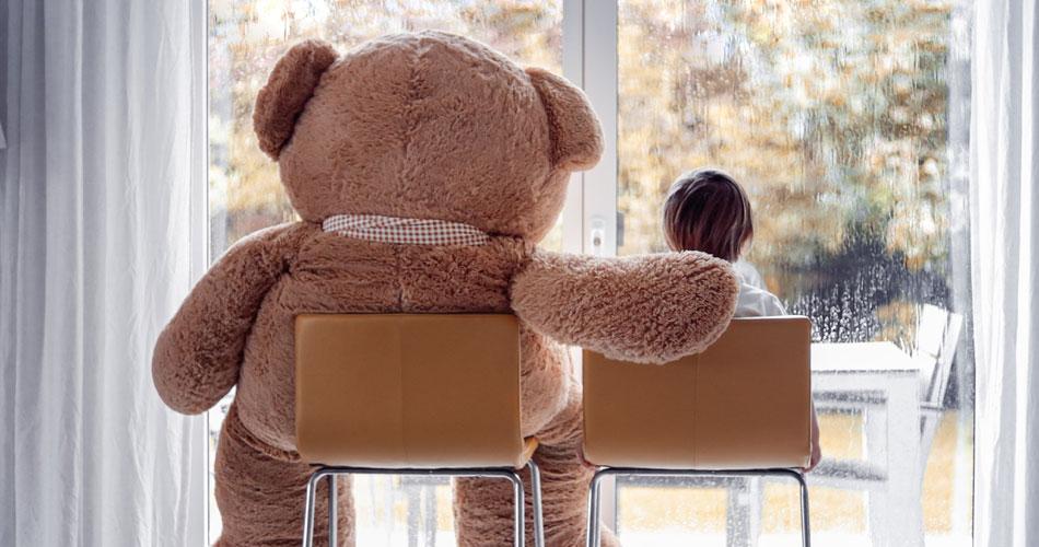 enfant assis devant une fenêtre avec un ours en peluche